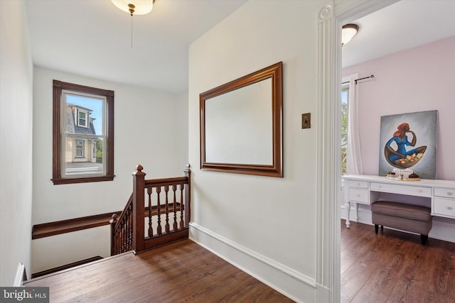 hallway with an upstairs landing, plenty of natural light, and dark wood-style floors