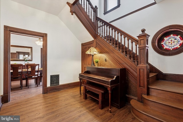 stairway featuring wood finished floors, a chandelier, lofted ceiling, and baseboards