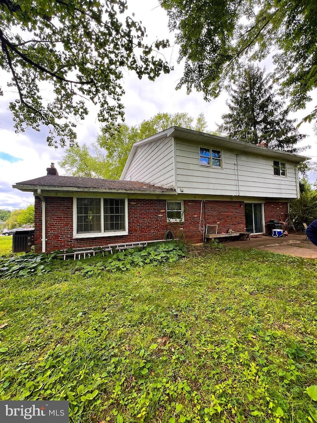 back of house with brick siding, a yard, a patio area, and a chimney