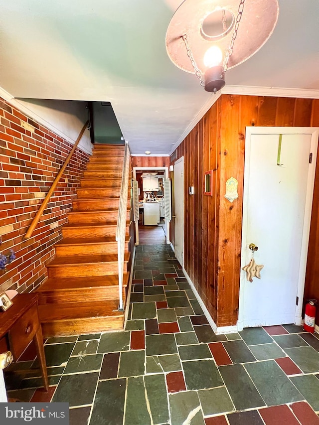 stairs with stone finish floors, ornamental molding, wooden walls, and baseboards