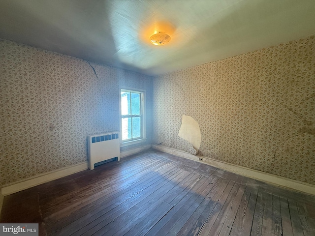 empty room featuring radiator heating unit, hardwood / wood-style flooring, wallpapered walls, and baseboards