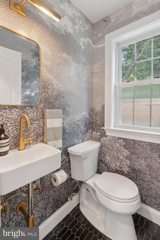 half bathroom with toilet, tile patterned floors, baseboards, a sink, and wallpapered walls