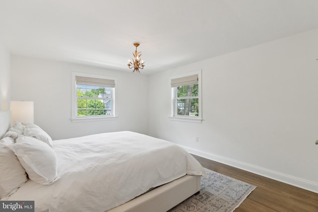 bedroom featuring multiple windows, baseboards, dark wood-type flooring, and a chandelier