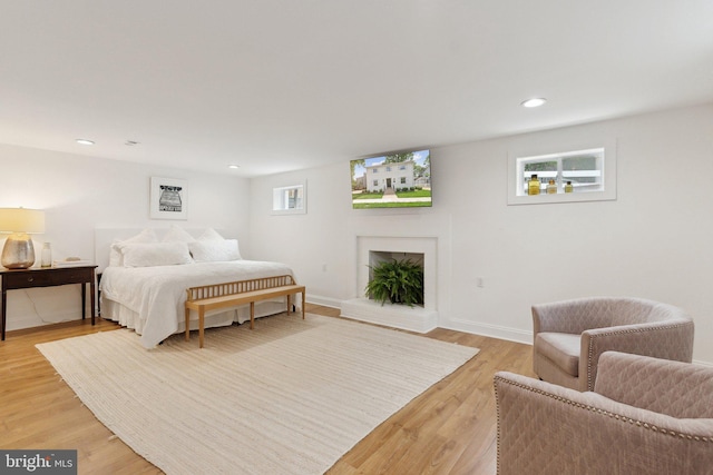 bedroom with a fireplace with raised hearth, light wood-style floors, recessed lighting, and baseboards