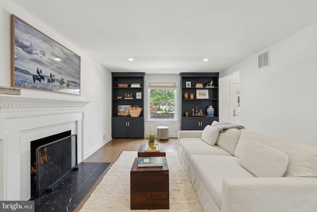 living room with wood finished floors, a high end fireplace, recessed lighting, baseboards, and built in features