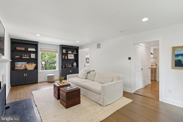 living room featuring dark wood finished floors, a fireplace with flush hearth, baseboards, recessed lighting, and built in shelves