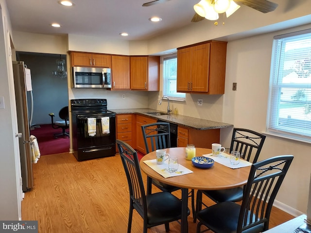 kitchen with appliances with stainless steel finishes, a sink, light wood-type flooring, brown cabinets, and healthy amount of natural light
