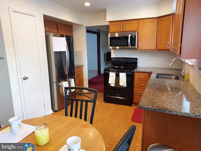 kitchen with stainless steel appliances, a sink, brown cabinetry, light wood-type flooring, and dark stone counters