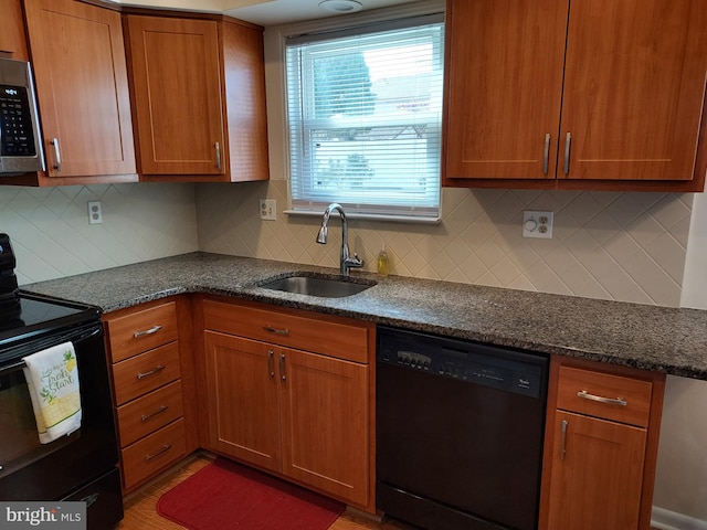 kitchen with black appliances, a sink, backsplash, brown cabinetry, and dark stone counters