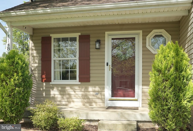 view of exterior entry with a shingled roof and a porch