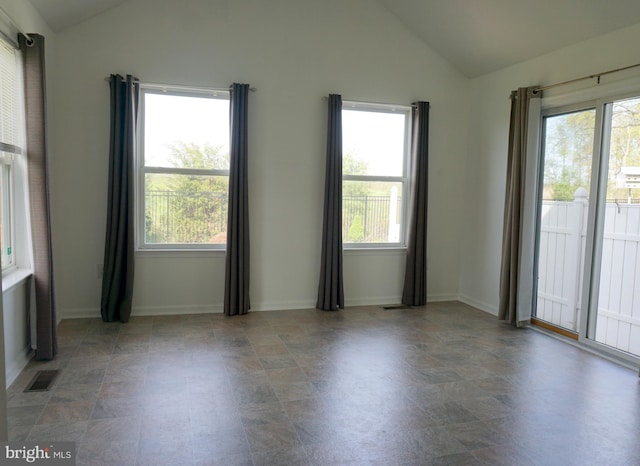 empty room with vaulted ceiling, healthy amount of natural light, baseboards, and stone finish flooring