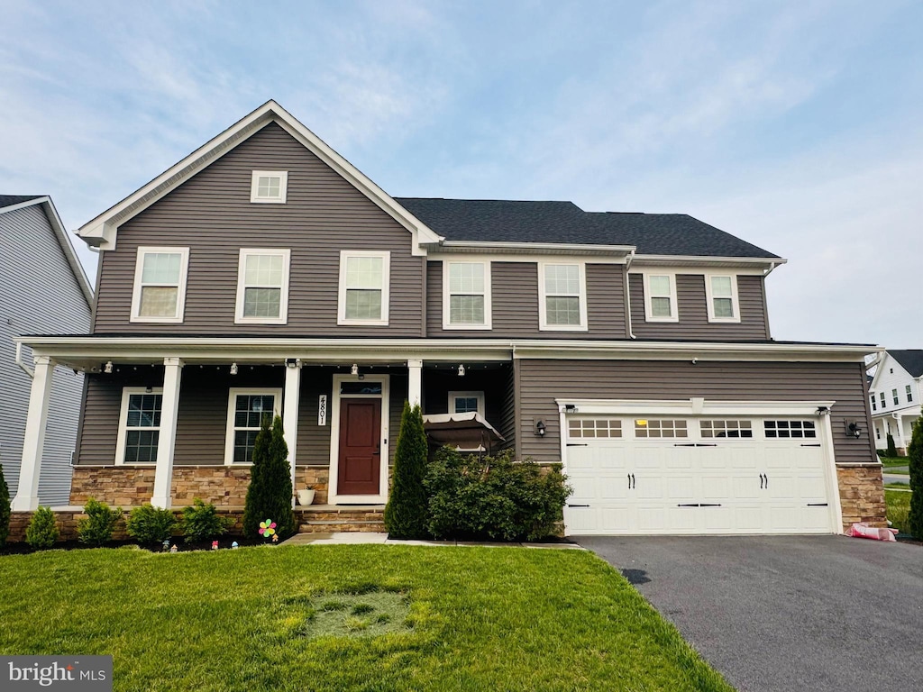 view of front of property with stone siding, asphalt driveway, a front yard, and a garage
