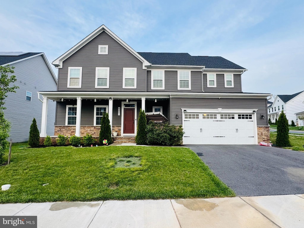 view of front facade featuring stone siding, driveway, an attached garage, a front yard, and covered porch