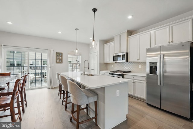 kitchen featuring appliances with stainless steel finishes, a sink, tasteful backsplash, light wood finished floors, and an island with sink