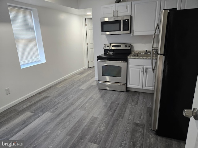 kitchen with stainless steel appliances, dark wood-style floors, white cabinetry, baseboards, and a sink