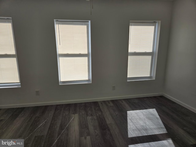 empty room featuring dark wood-style flooring, baseboards, and healthy amount of natural light