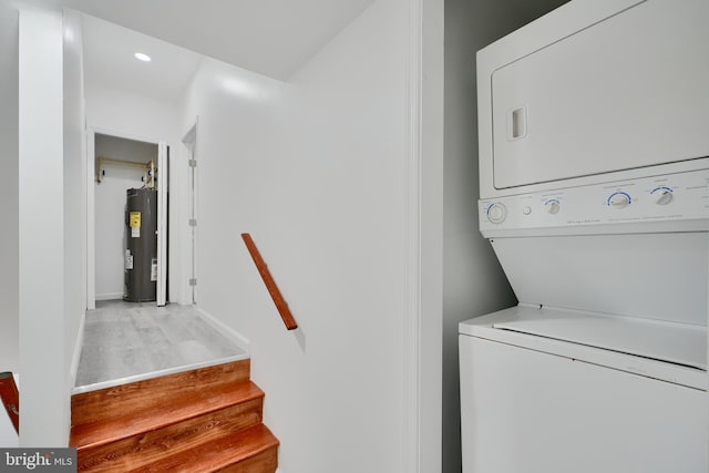 clothes washing area featuring electric water heater, stacked washer / drying machine, light wood-style floors, recessed lighting, and baseboards