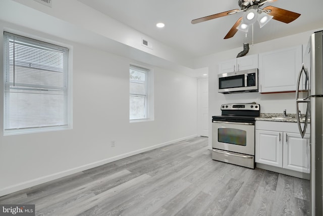 kitchen featuring appliances with stainless steel finishes, light wood-style flooring, white cabinetry, ceiling fan, and baseboards