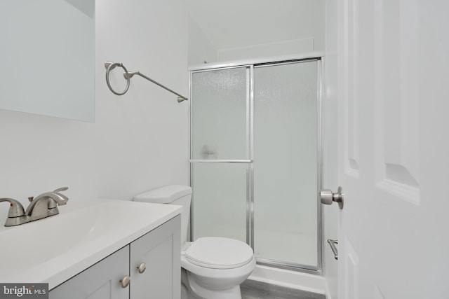 bathroom with a stall shower, toilet, vanity, and wood finished floors