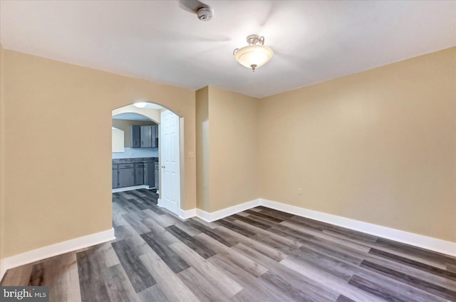 spare room with arched walkways, dark wood finished floors, baseboards, and a smoke detector