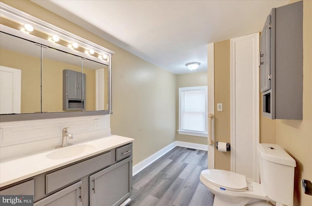 bathroom featuring toilet, decorative backsplash, vanity, wood finished floors, and baseboards