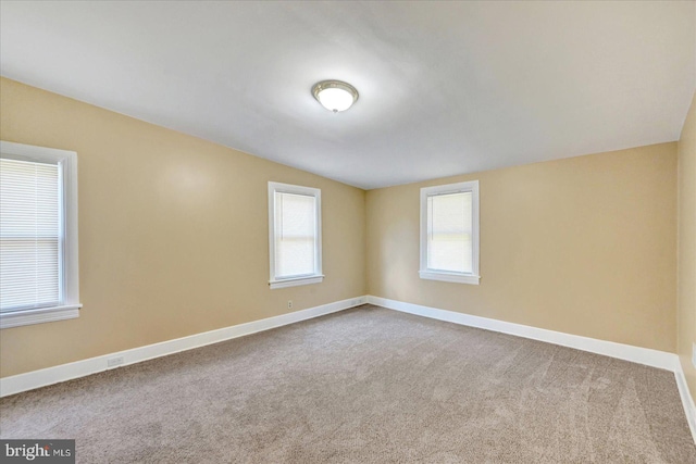 carpeted empty room with baseboards and vaulted ceiling