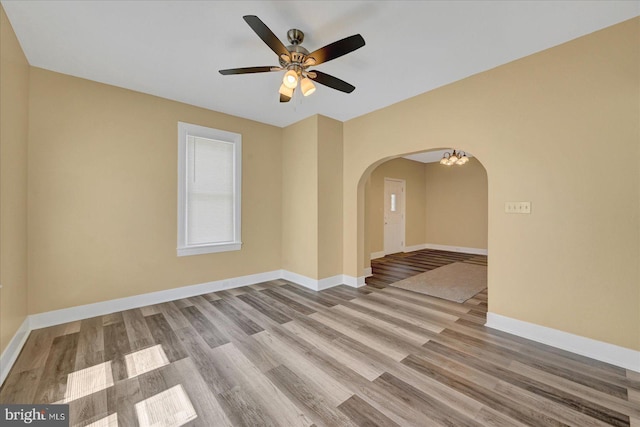 empty room with arched walkways, wood finished floors, baseboards, and ceiling fan