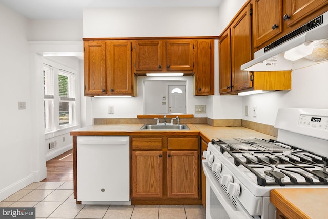 kitchen with white appliances, under cabinet range hood, a sink, brown cabinetry, and light tile patterned floors