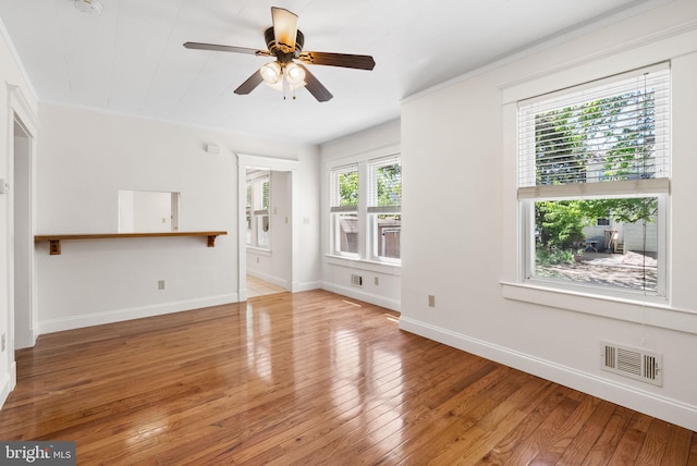 unfurnished living room featuring hardwood / wood-style floors, ceiling fan, baseboards, and crown molding