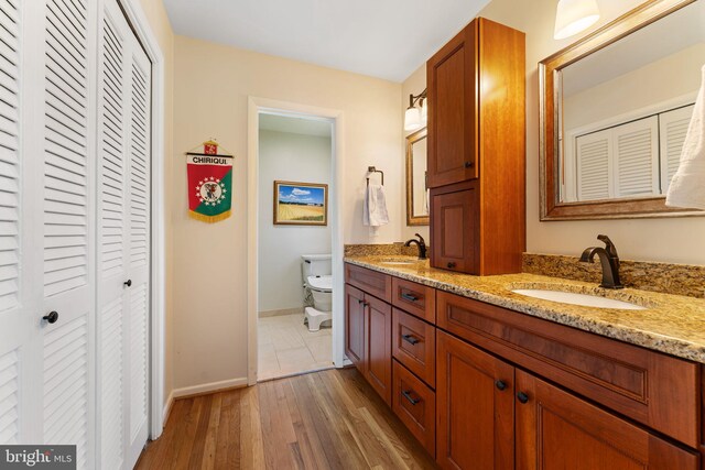 bathroom featuring a closet, double vanity, toilet, and baseboards