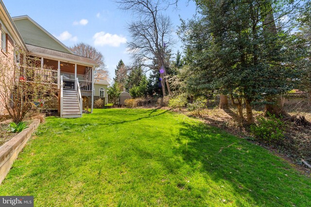 view of grassy yard with stairway, a storage shed, an outbuilding, and a sunroom