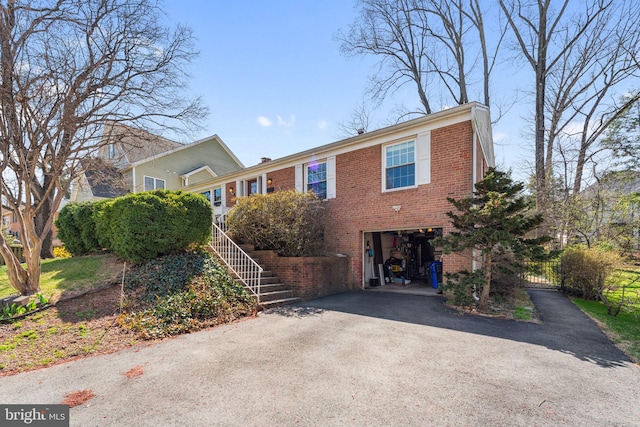 view of front of property featuring asphalt driveway, a garage, brick siding, fence, and stairway
