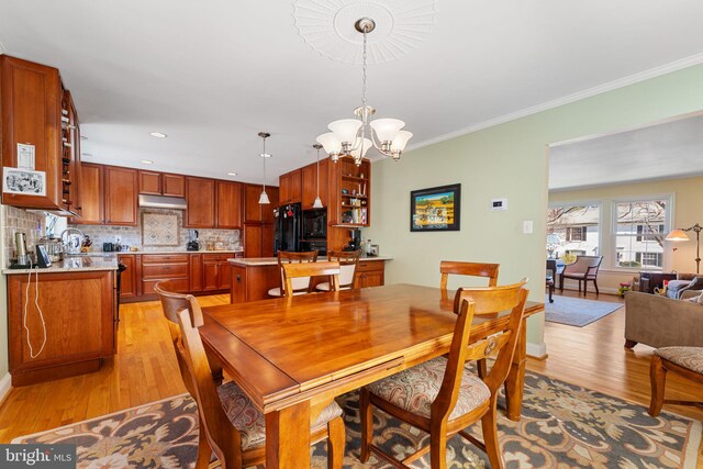 dining room featuring light wood finished floors, a chandelier, crown molding, and baseboards