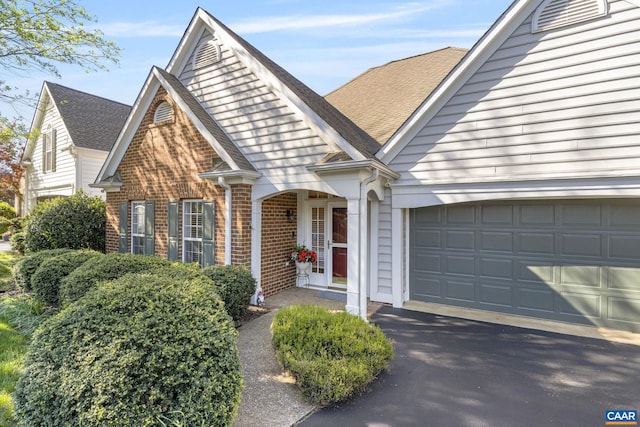 view of front of home with brick siding, an attached garage, asphalt driveway, and a shingled roof