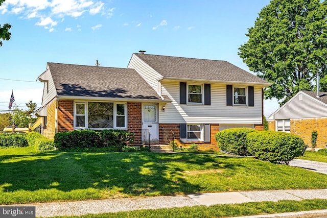 tri-level home with brick siding, a front yard, and roof with shingles
