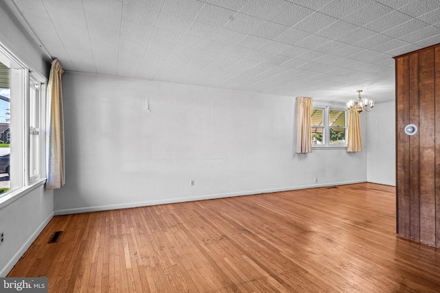 unfurnished room with a chandelier, light wood finished floors, and baseboards
