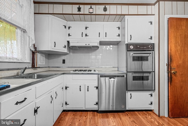 kitchen with double oven, stainless steel dishwasher, under cabinet range hood, a sink, and light wood-type flooring