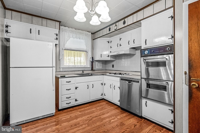 kitchen featuring stainless steel appliances, a chandelier, under cabinet range hood, and white cabinetry
