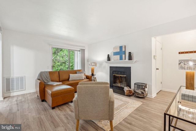 living room with a fireplace with flush hearth, light wood finished floors, and baseboards