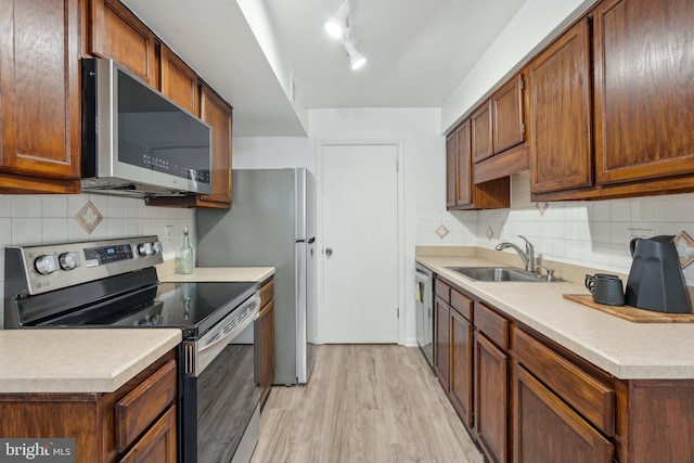 kitchen featuring appliances with stainless steel finishes, a sink, light wood-style floors, and backsplash