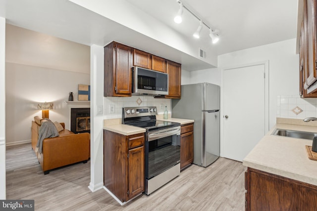 kitchen with stainless steel appliances, a sink, tasteful backsplash, and a glass covered fireplace