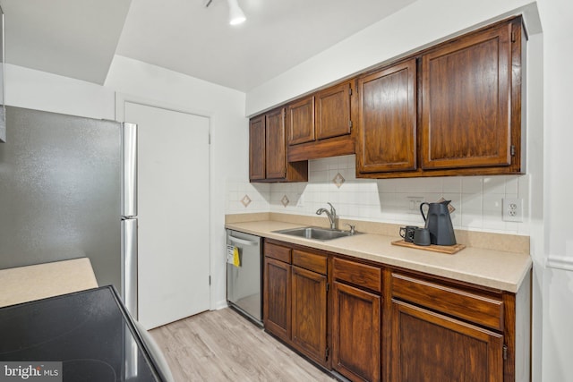 kitchen featuring appliances with stainless steel finishes, a sink, light wood-style floors, tasteful backsplash, and light countertops