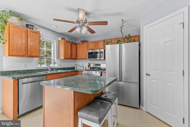 kitchen with stainless steel appliances, a sink, a ceiling fan, dark countertops, and a kitchen breakfast bar