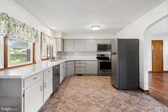 kitchen featuring appliances with stainless steel finishes, a sink, arched walkways, gray cabinets, and light countertops