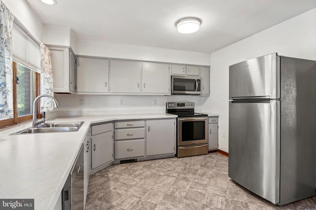 kitchen with stainless steel appliances, gray cabinetry, a sink, and light countertops