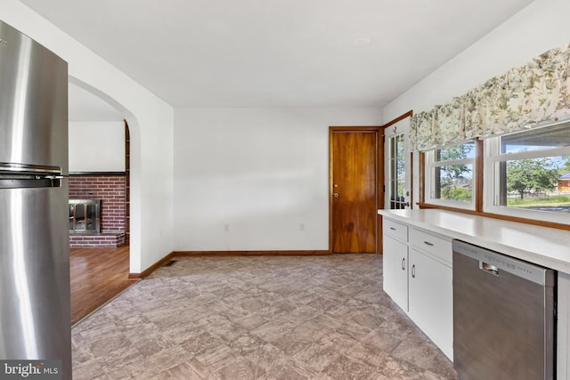 kitchen with appliances with stainless steel finishes, light countertops, a brick fireplace, white cabinetry, and arched walkways