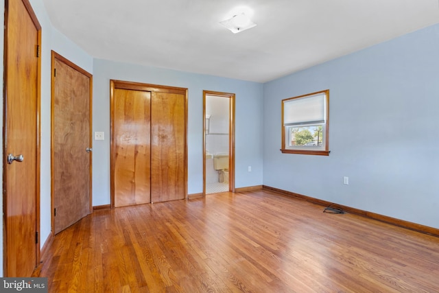unfurnished bedroom with light wood-style flooring, baseboards, and connected bathroom