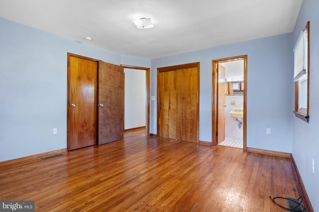 unfurnished bedroom with wood finished floors, baseboards, and ensuite bathroom
