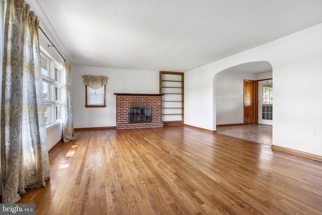 unfurnished living room featuring arched walkways, wood finished floors, a fireplace, and baseboards