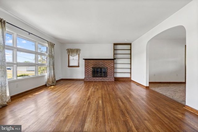 unfurnished living room with wood finished floors, arched walkways, baseboards, a fireplace, and built in features